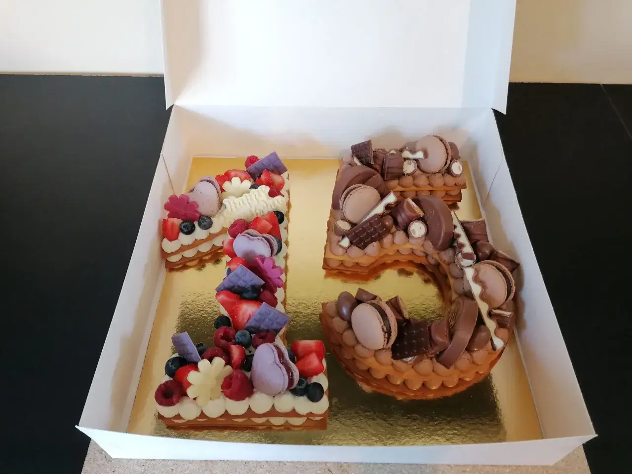Un délicieux number cake 16, orné de fruits rouges frais et de chocolats gourmands, prêt à être dégusté.