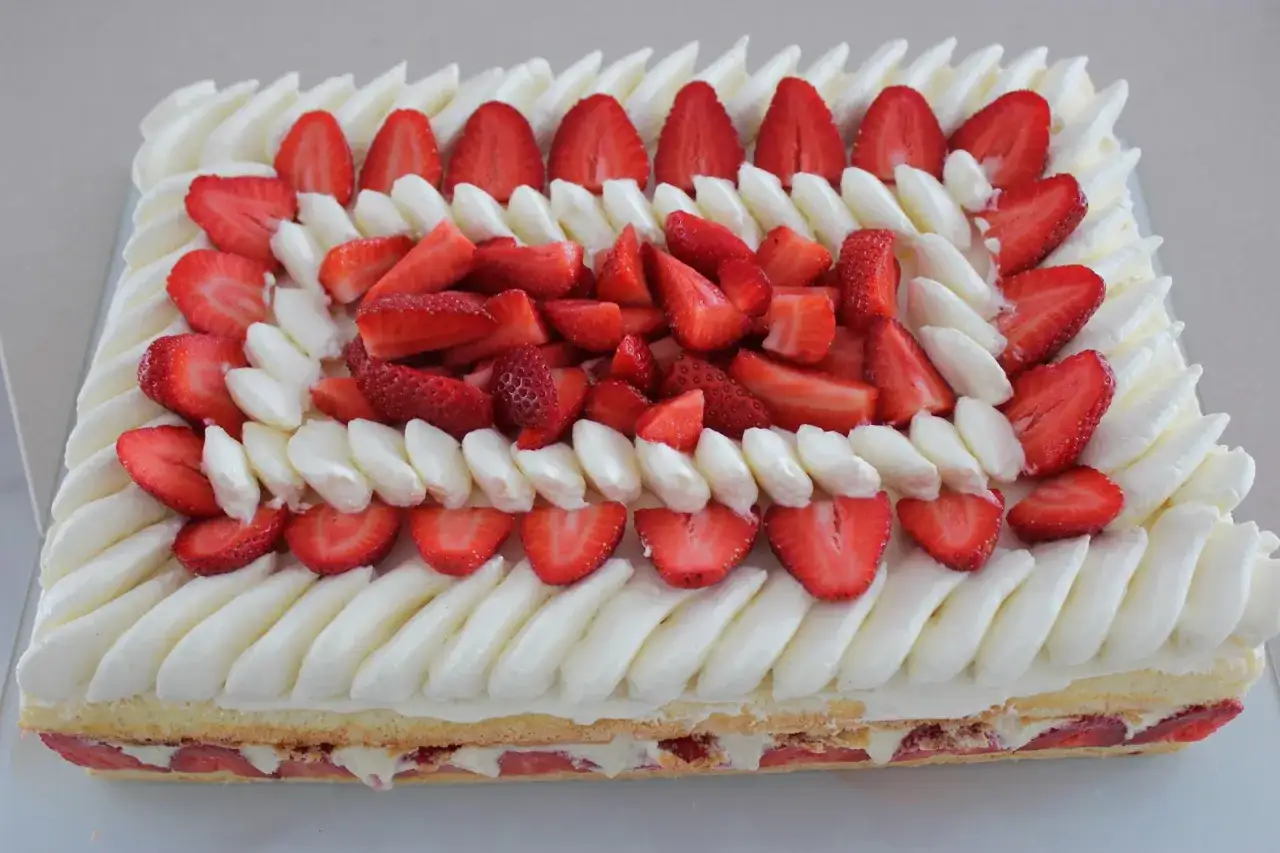 Un fraisier rectangulaire pour 20 personnes, décoré de fraises fraîches et de crème fouettée en rosaces.