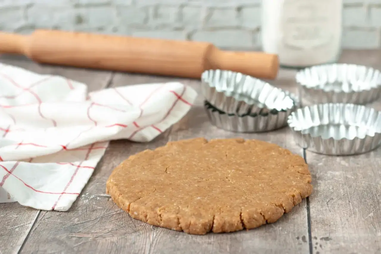 Pâte sablée prête pour la cuisson au four à chaleur tournante. Rouleau à pâtisserie, moules et torchon à proximité.