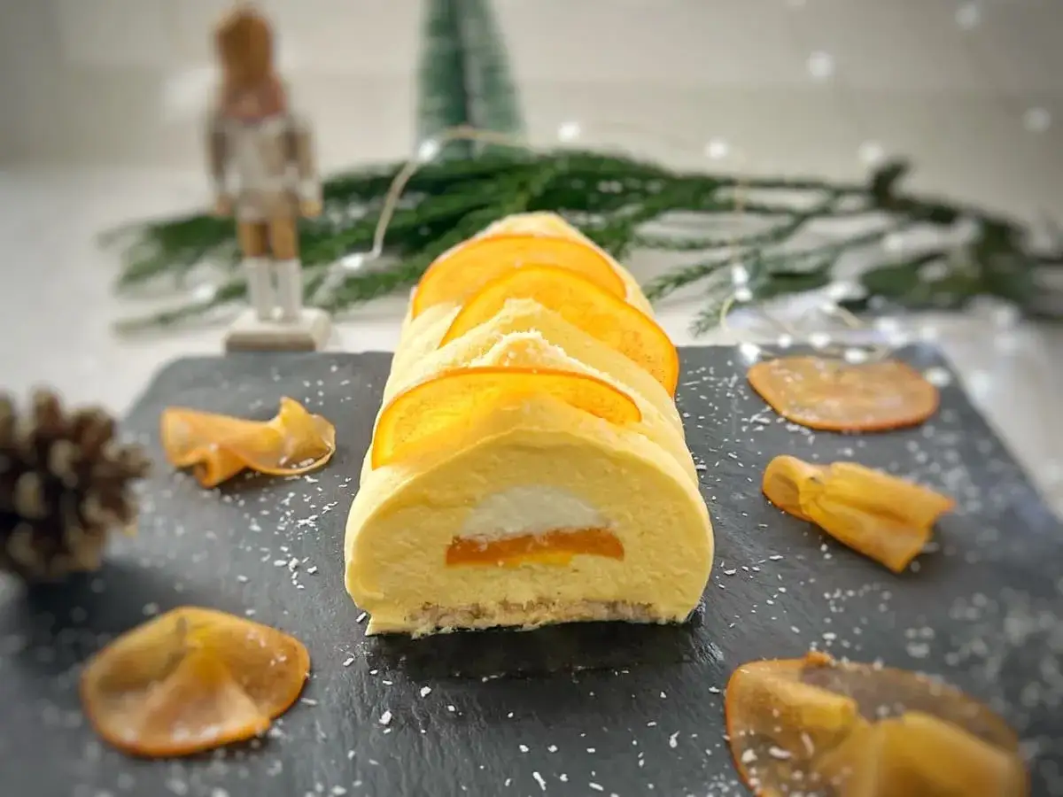 Bûche de Noël aux fruits exotiques, décorée de fines tranches d'orange et de fruits séchés. Une gourmandise festive et ensoleillée.