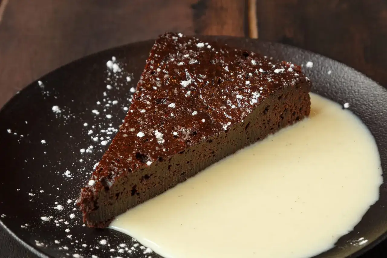 Tranche de gâteau au chocolat moelleux et facile, saupoudrée de sucre glace, servie avec une crème anglaise onctueuse.