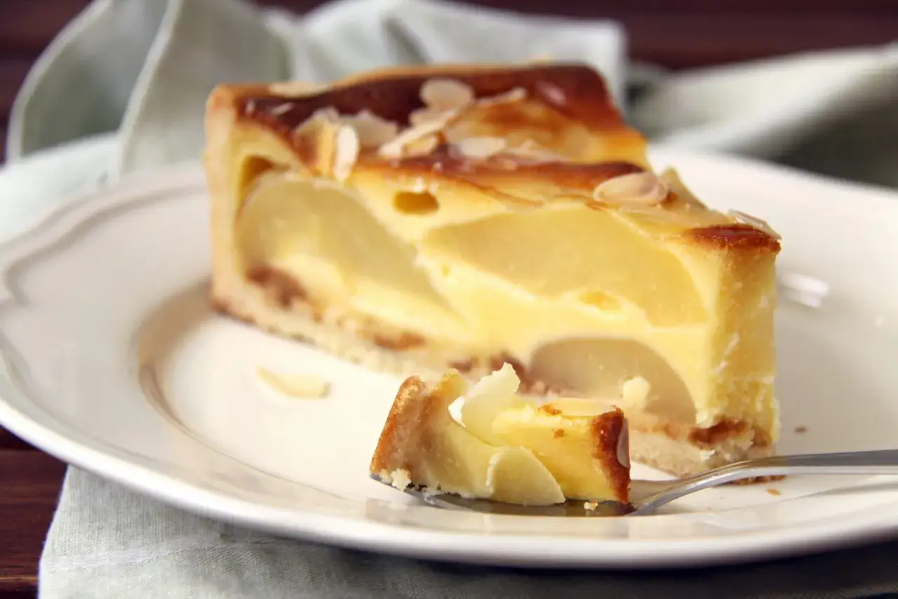 Une part de tarte aux poires au sirop, garnie d'amandes effilées, sur une assiette blanche.