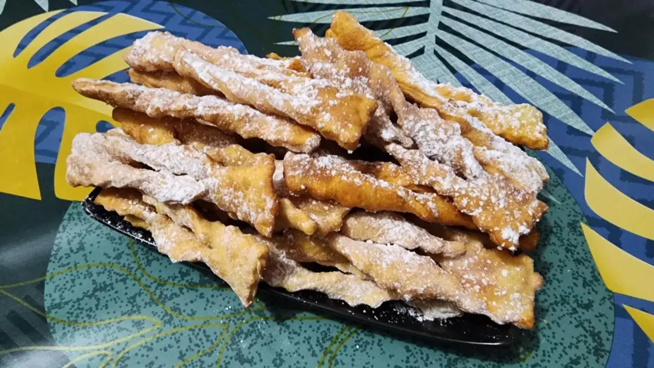 Des merveilles bien gonflées, saupoudrées de sucre glace, sur une assiette noire. Un délice croustillant prêt à être dégusté.