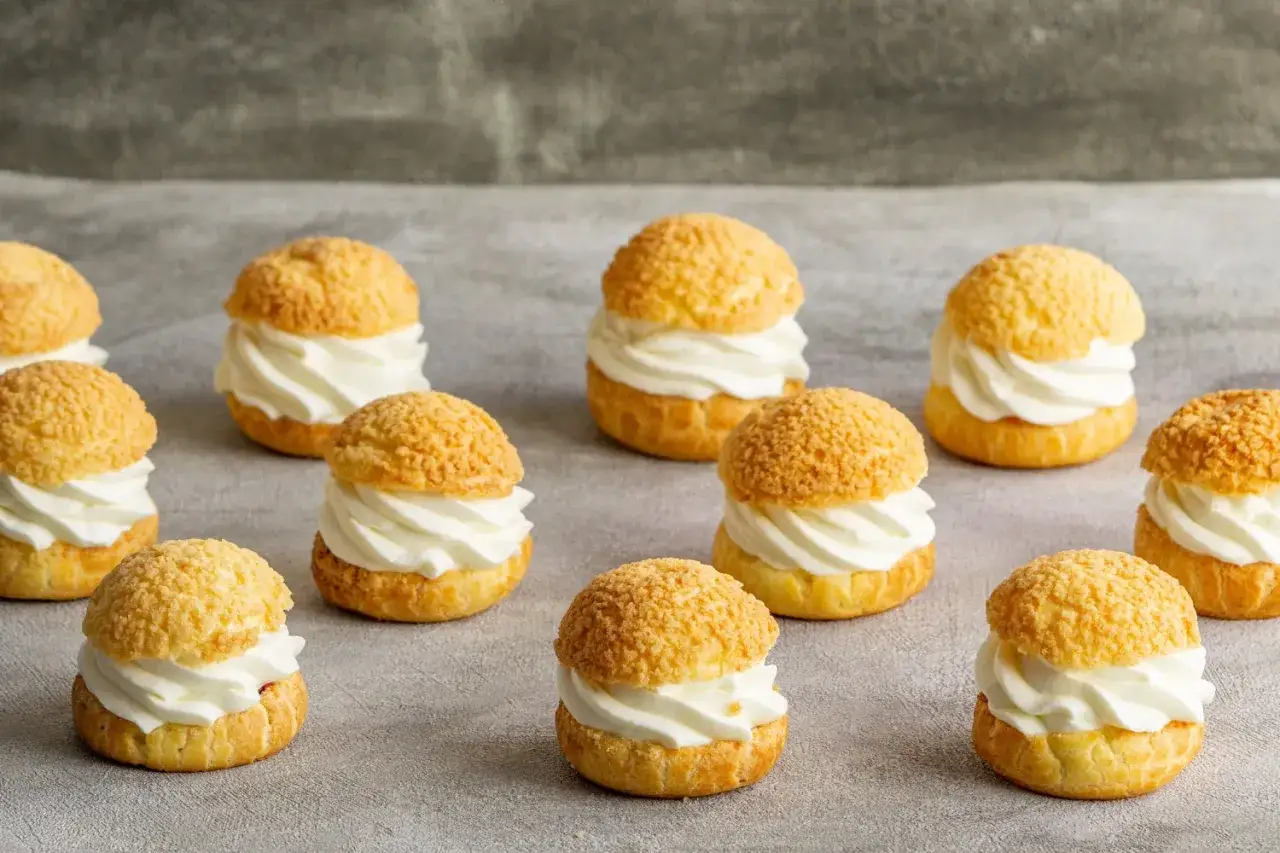 Douze choux garnis de crème fouettée, prêts à être dégustés après leur cuisson parfaite.