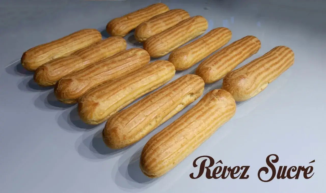 Douze éclairs dorés, prêts à être garnir. La pâte à choux est parfaitement cuite, prête pour un rêve sucré.