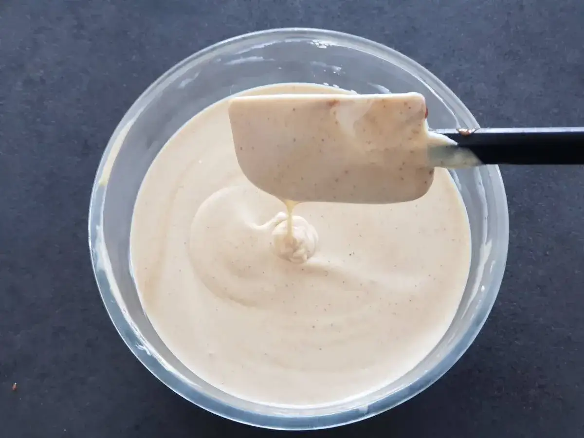 Une spatule retire une portion de mousse praliné onctueuse d'un bol en verre.