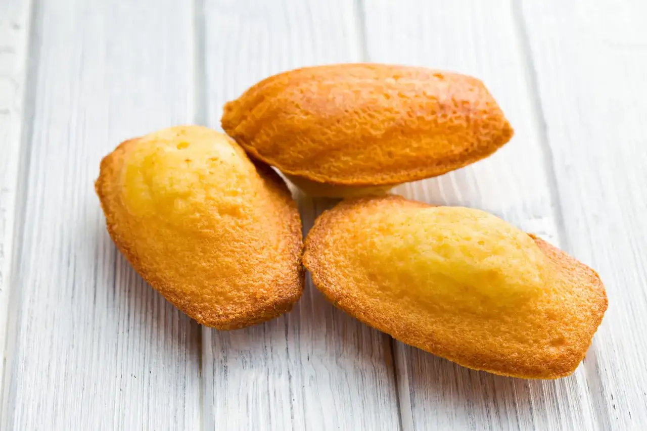 Trois biscuits madeleine dorés, faits maison avec le Thermomix, sur un fond de bois clair.