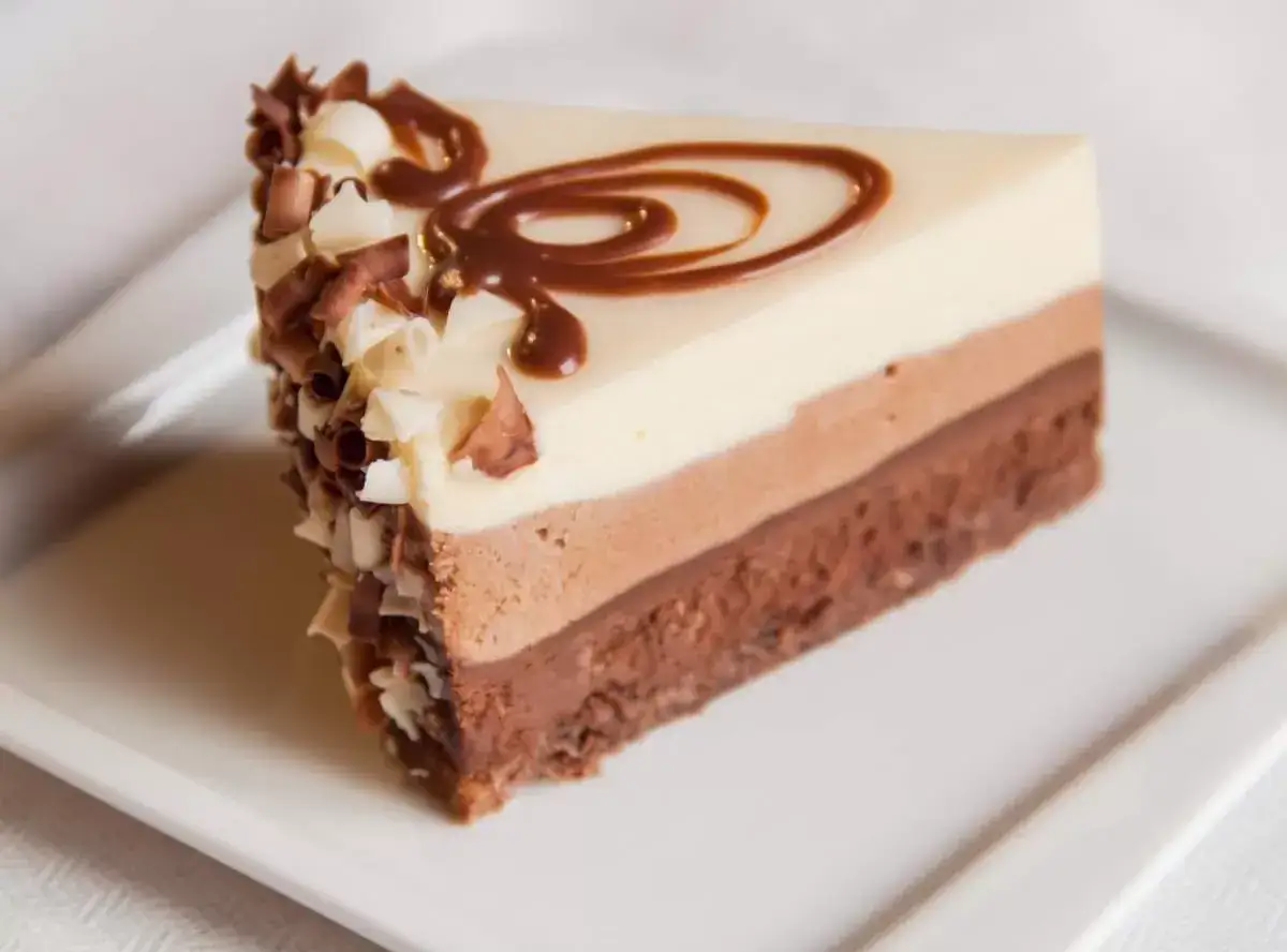 Tranche de gâteau triple chocolat, avec des copeaux de chocolat blanc et noir, et un tourbillon de chocolat sur le dessus. Un délice croustillant gavotte chocolat.