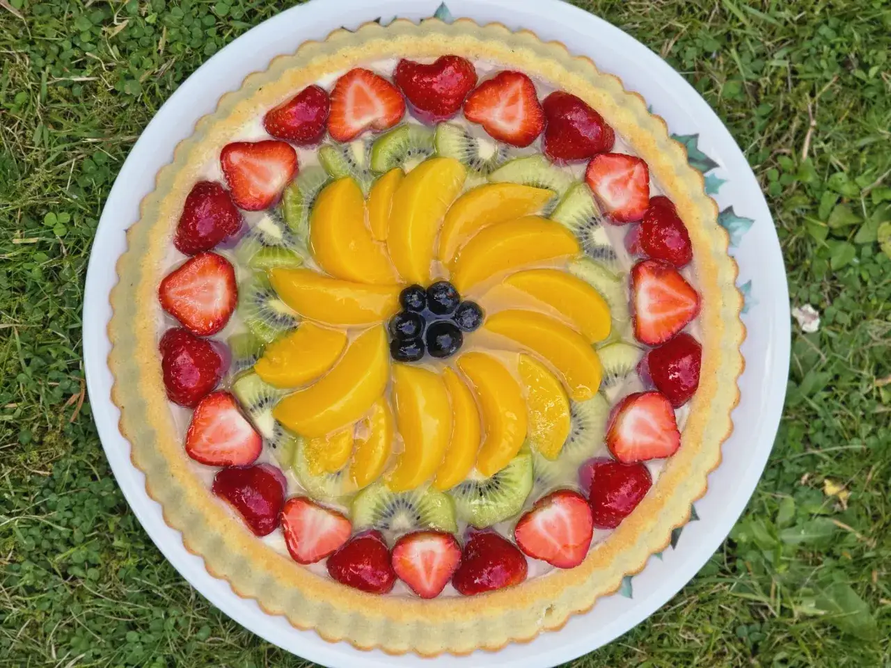 Délicieuse décoration tarte aux fruits : fraises, kiwis, pêches et myrtilles disposés en rosace sur une pâte dorée.