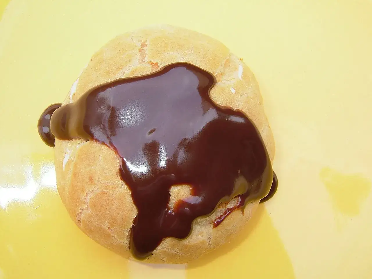 Un délice de profiteroles vraie recette, nappé d'une sauce au chocolat onctueuse sur fond jaune.