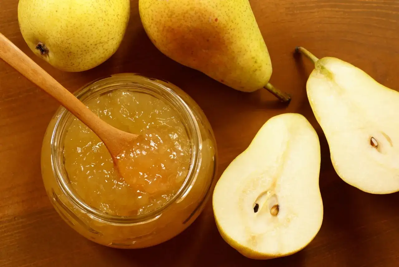 Un pot de confiture de poires maison, avec une cuillère en bois, entouré de poires fraîches coupées en deux.