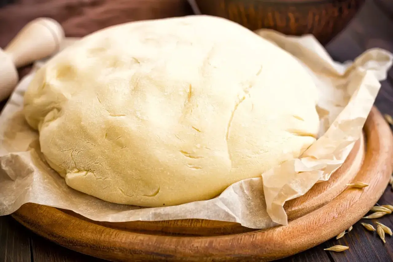 Une boule de pâte brisée à l'ancienne, prête à être travaillée, repose sur du papier sulfurisé, sur une planche en bois.