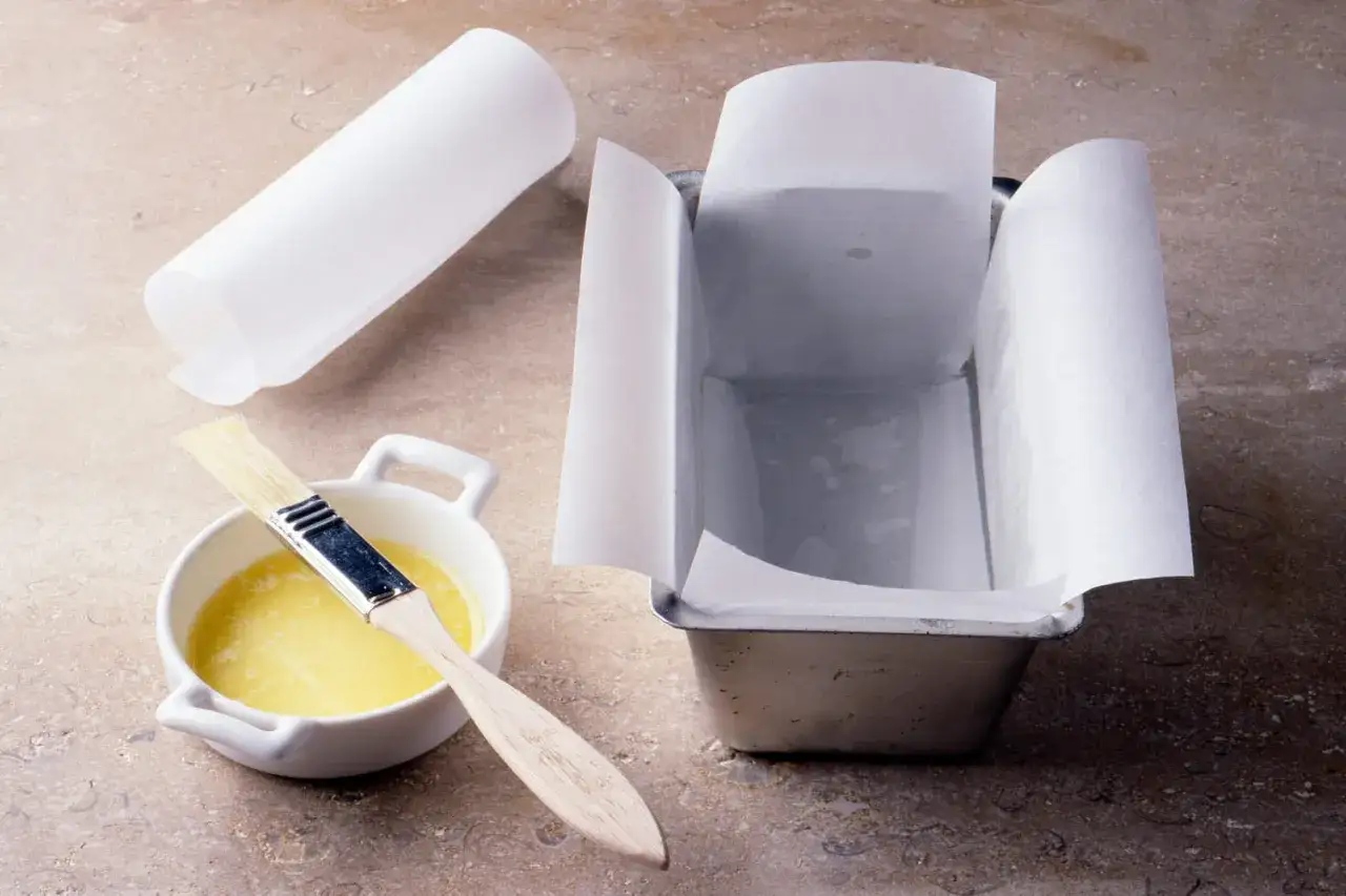 Préparation pour chemiser un moule : papier sulfurisé, beurre fondu et pinceau sur un plan de travail.
