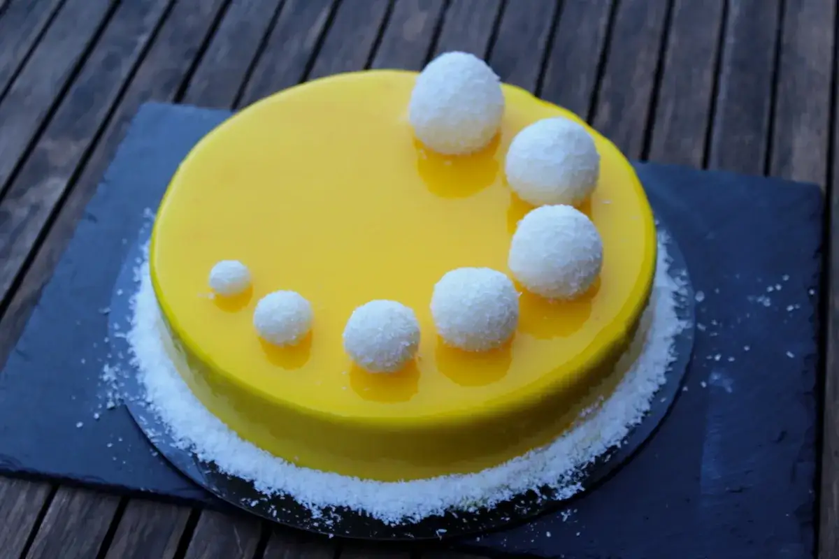 Gâteau rond jaune vif, décoré de boules de coco et de noix de coco râpée. Une recette insert citron pour un dessert acidulé.