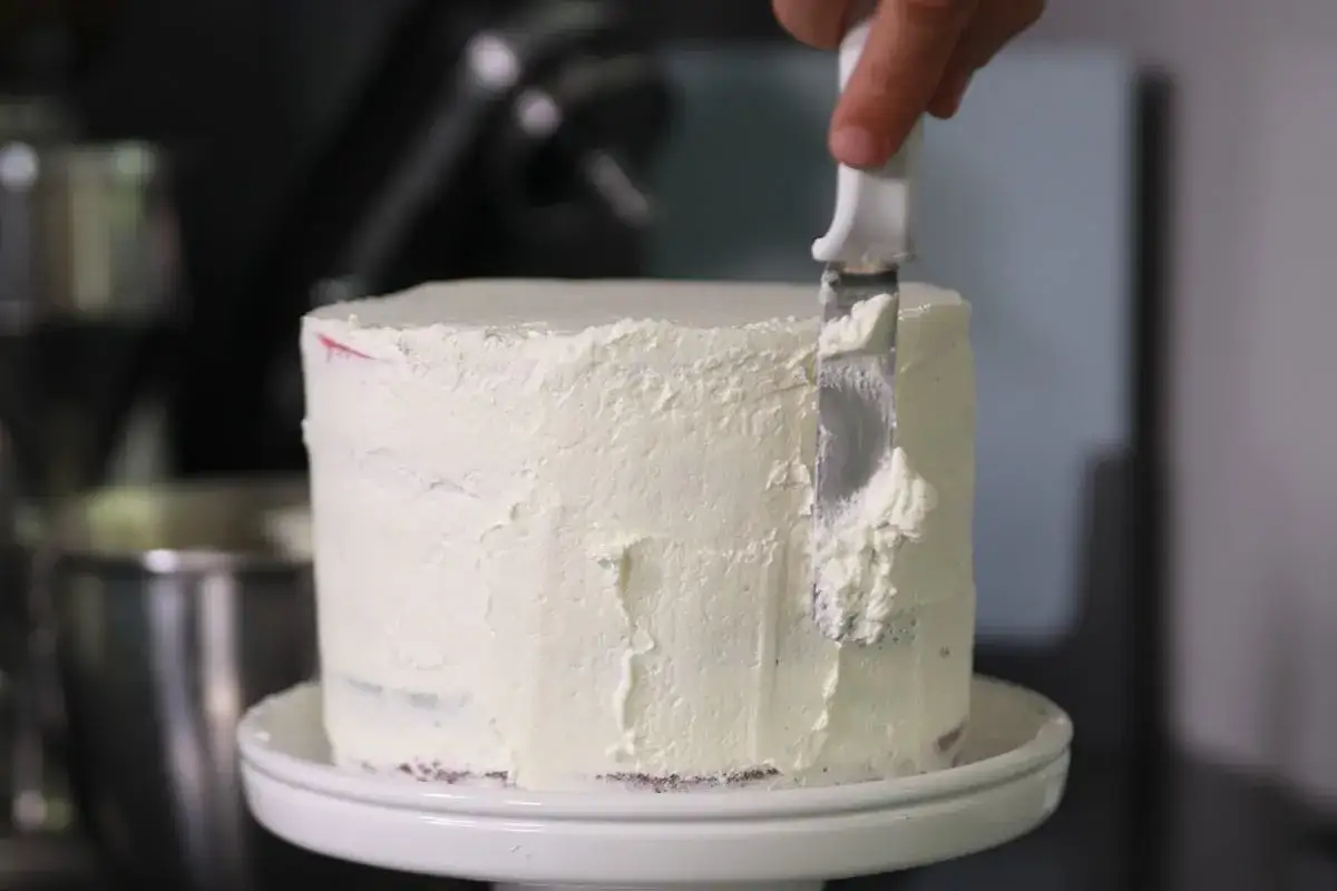 Application d'une couche de crème chantilly sur un gâteau. La spatule lisse la texture aérienne.
