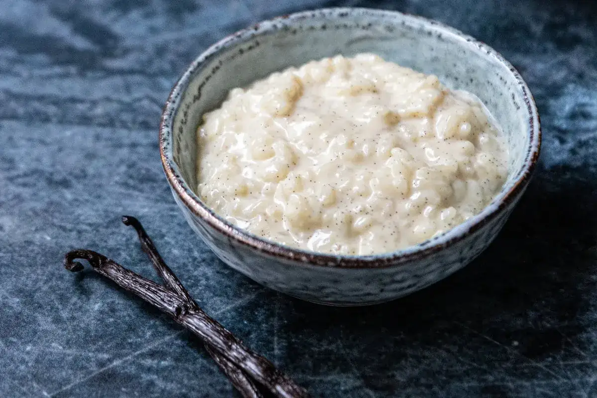 Un bol de riz au lait crémeux, parsemé de points de vanille, avec deux gousses de vanille à côté.