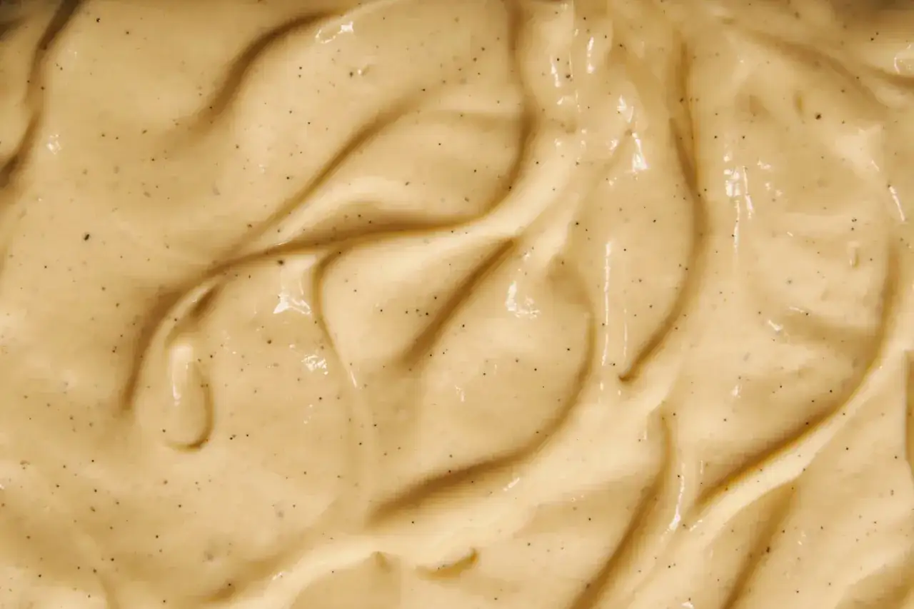 Texture onctueuse de crème pâtissière à la vanille, avec des points noirs de vanille. La texture suggère l'ajout de gélatine pour une tenue parfaite.