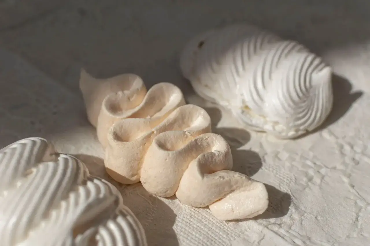 Trois meringues, dont une en forme de ruban, sur un tissu blanc. La meringue italienne, l&eacute;g&egrave;re et a&eacute;rienne, invite &agrave; la gourmandise.