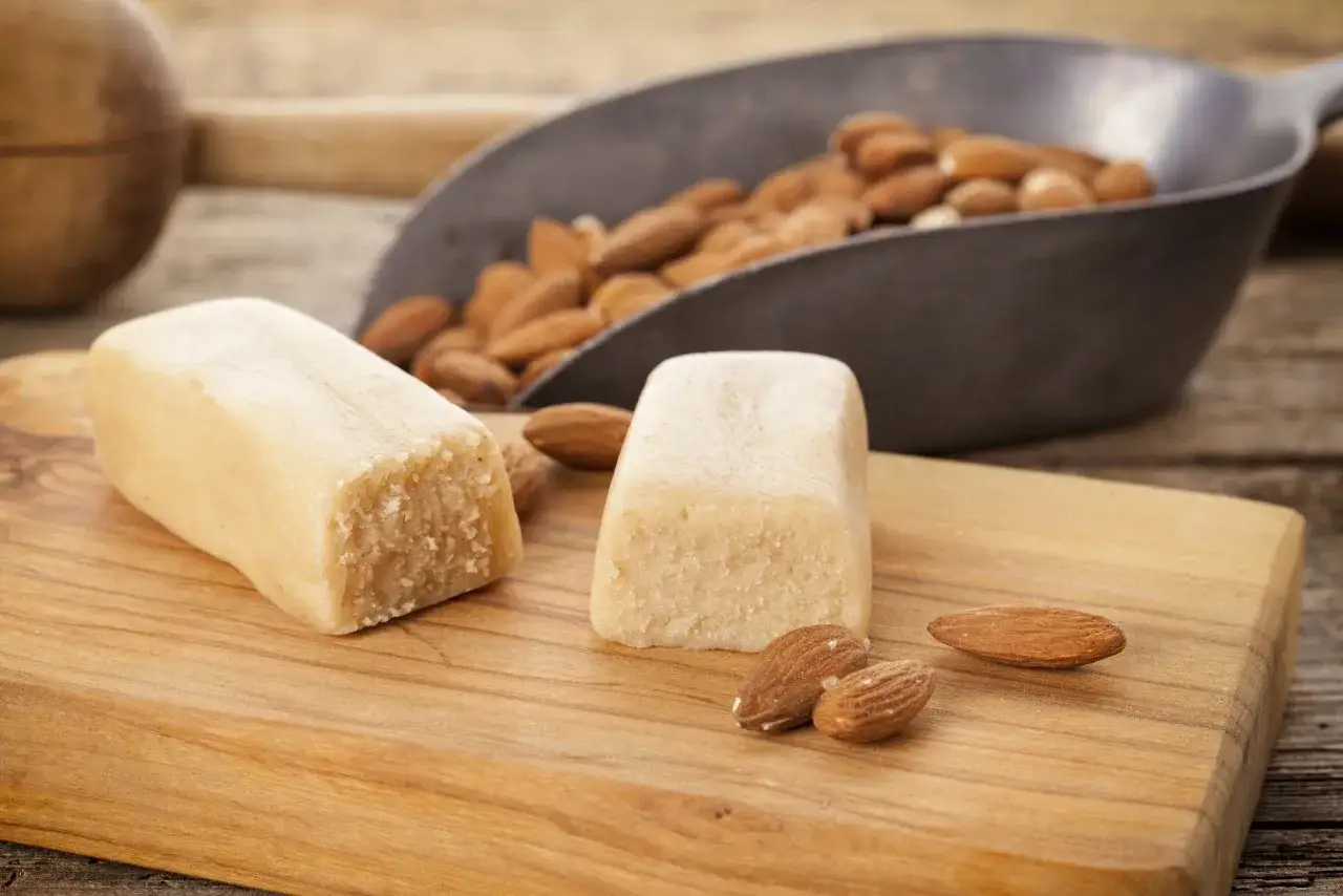 Deux blocs de pâte d'amande et des amandes entières sur une planche en bois. Idéal pour une recette pâte d'amande maison.