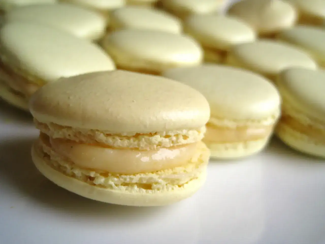 Un macaron meringue italienne, délicatement garni d'une crème onctueuse, se tient au premier plan, entouré d'autres douceurs pâles.
