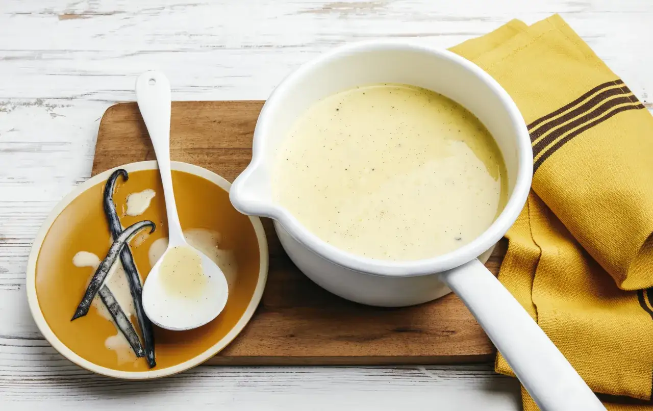 Une casserole de crème anglaise 1 litre, prête à être servie. Des gousses de vanille sur une assiette à côté.