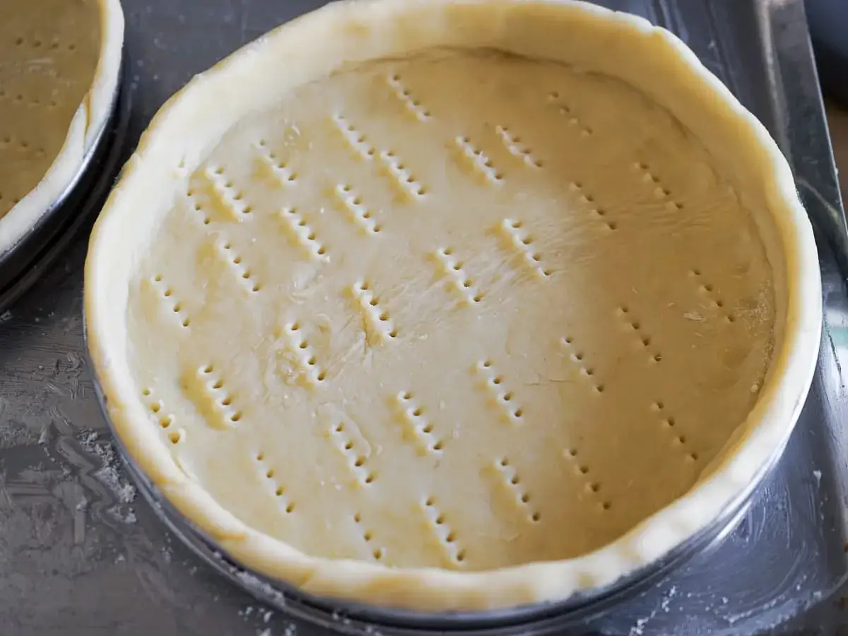 Pâte sablée prête pour la cuisson, piquée de trous pour une dorure parfaite.