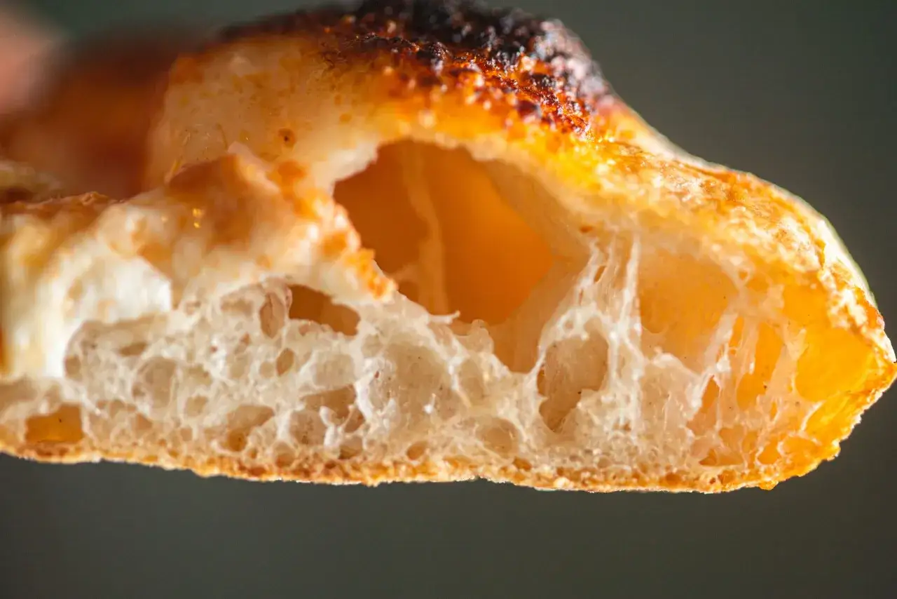 Gros plan sur la mie aérée d'une pâte à pizza professionnelle, avec une croûte dorée et légèrement brûlée.