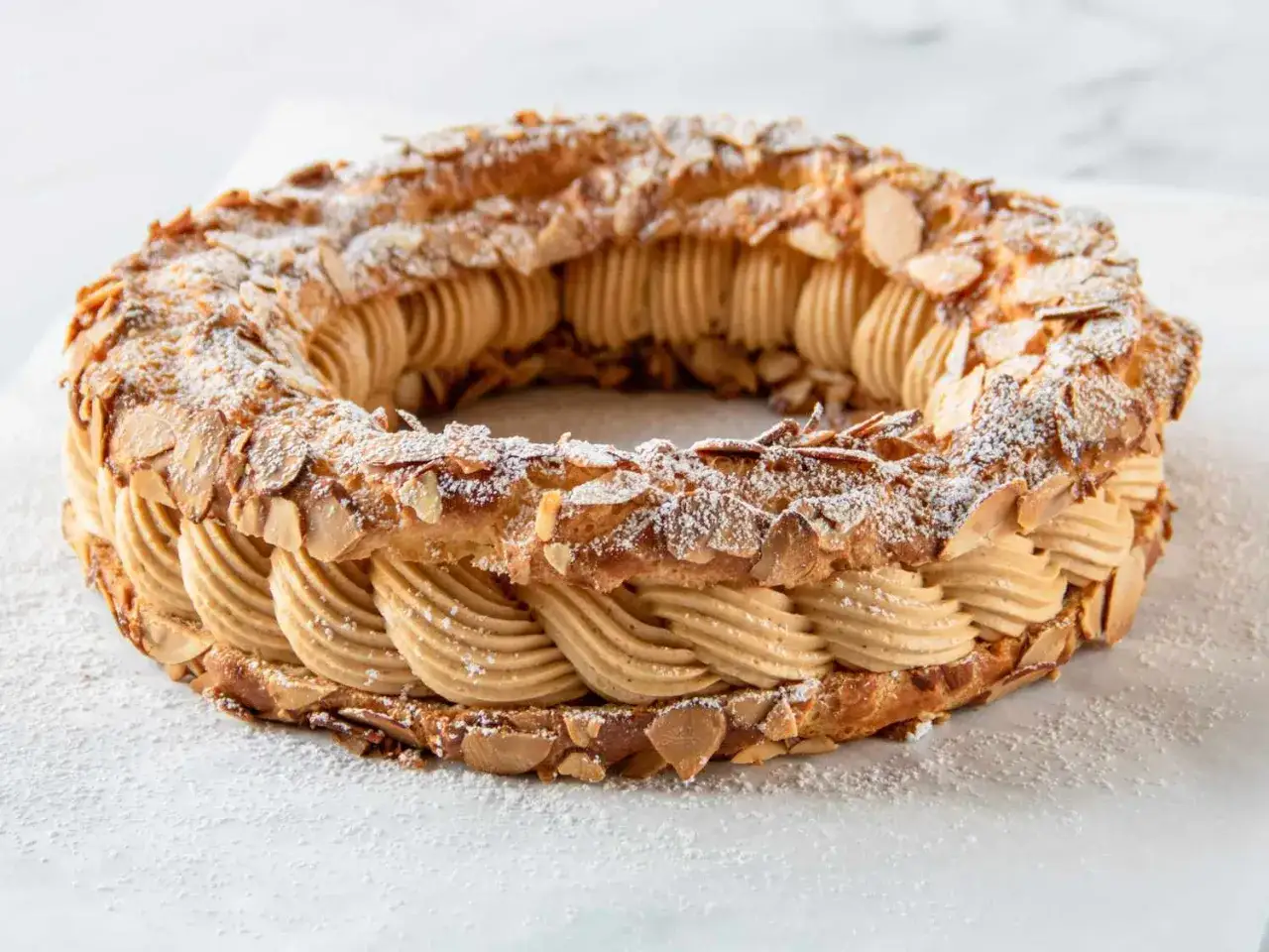 Un Paris-Brest rond, garni d'une crème onctueuse au praliné et parsemé d'amandes effilées et de sucre glace.