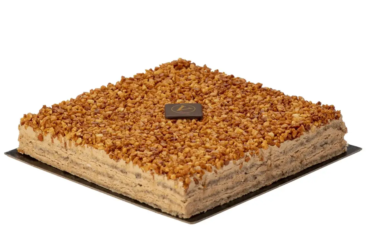 Un délicieux gâteau russe, carré et généreusement garni de noisettes caramélisées, avec un médaillon chocolat au centre.