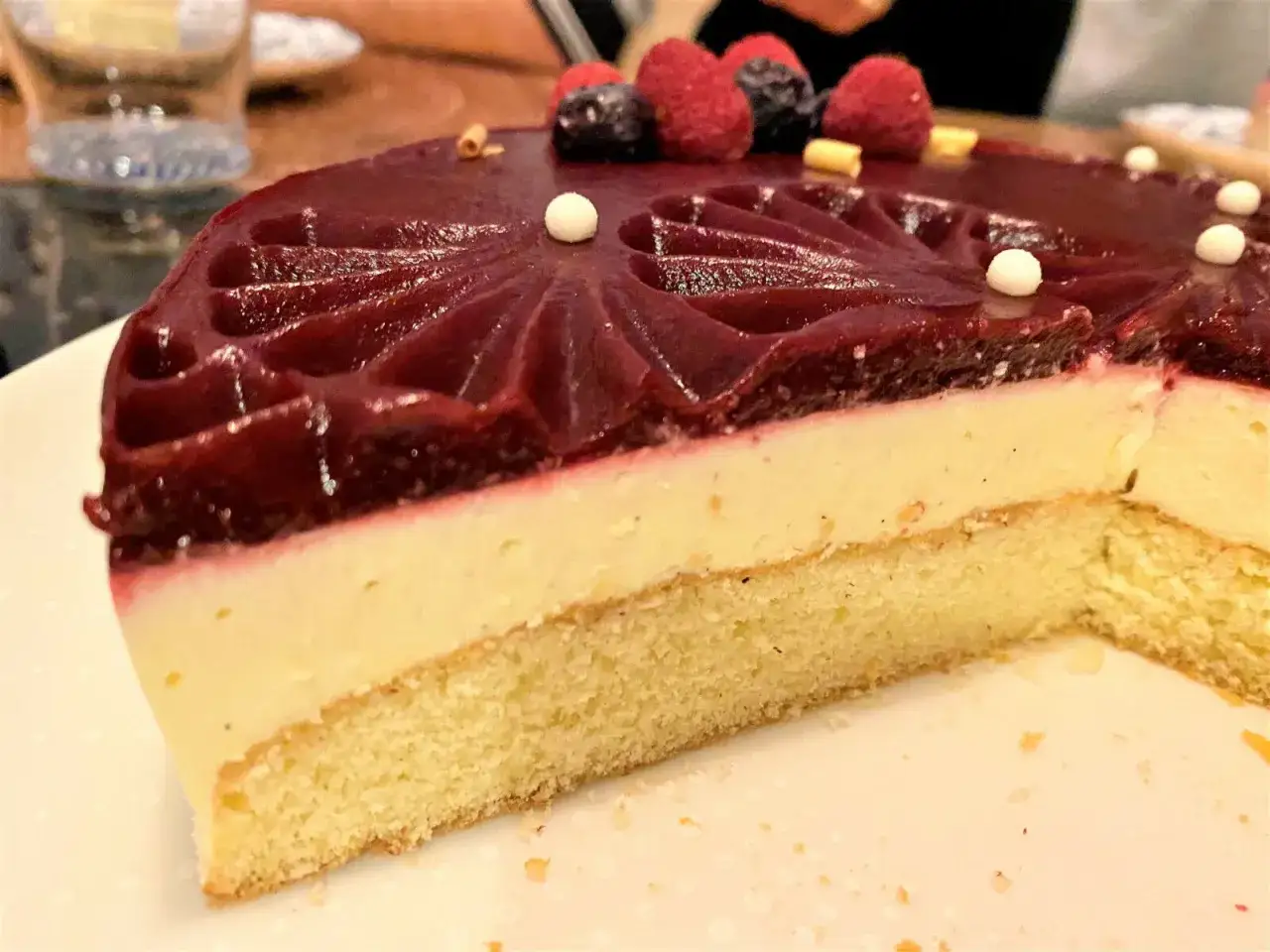 Tranche d'entremet avec biscuit madeleine, mousse légère et glaçage aux fruits rouges, décoré de baies fraîches.