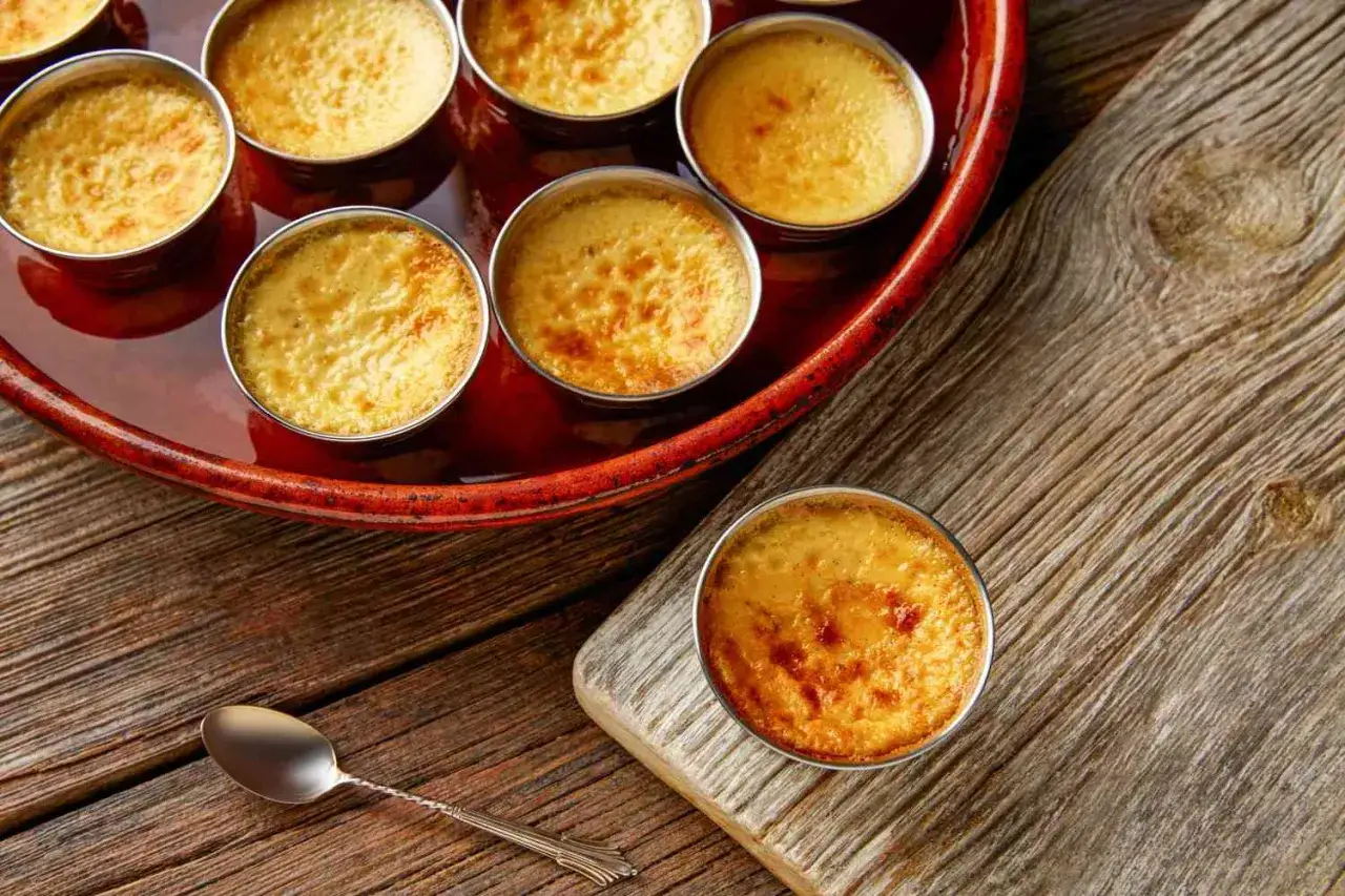 Crème brûlée dorée, résultat d'une cuisson bain-marie au four. Une cuillère repose sur le bois.