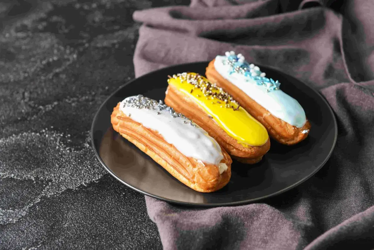 Trois éclairs colorés sur une assiette noire, parfaits pour une recette pâte à choux éclair réussie.