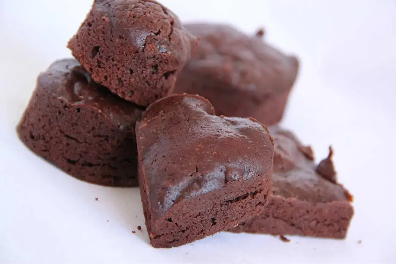 Un tas de financiers au chocolat, certains en forme de cœur, sur fond blanc.