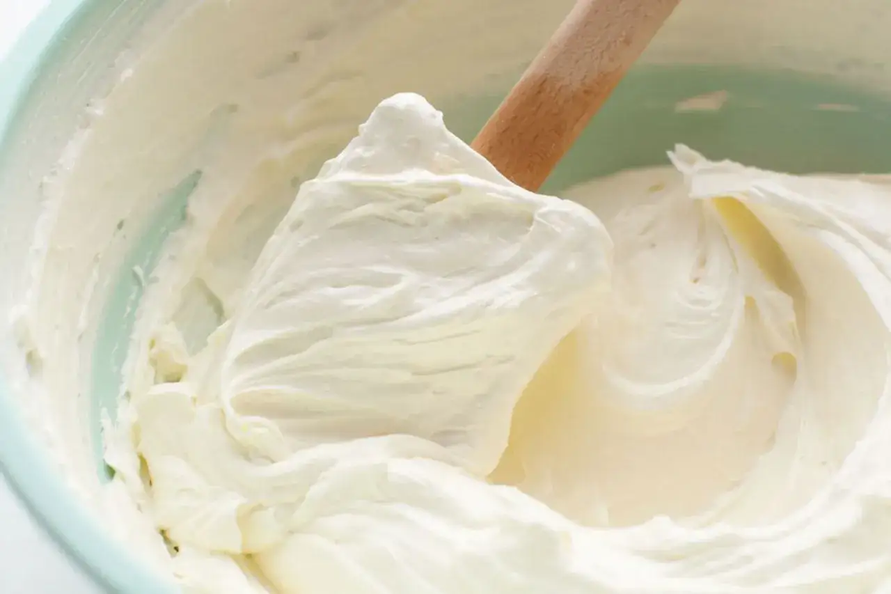 Une spatule en bois mélange une crème au beurre professionnelle onctueuse dans un bol vert pâle.