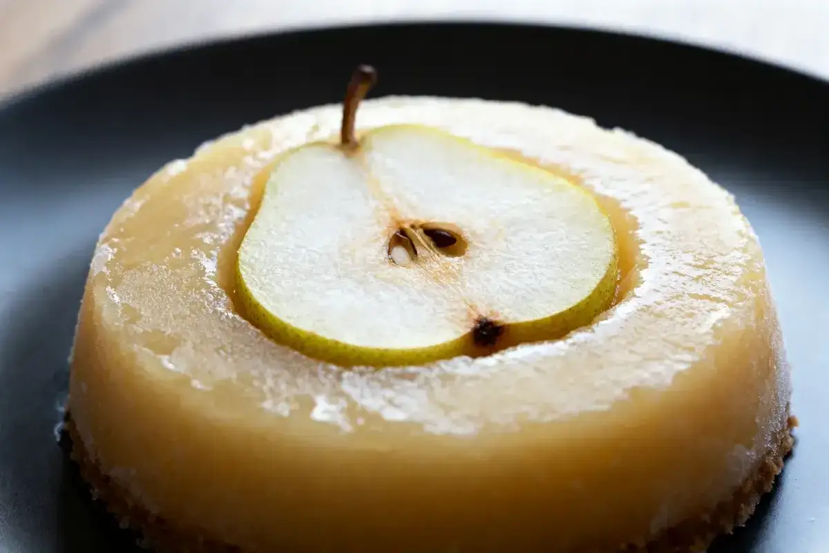 Un délicieux entremet poire, glacé et orné d'une fine tranche de poire fraîche, sur une assiette noire.