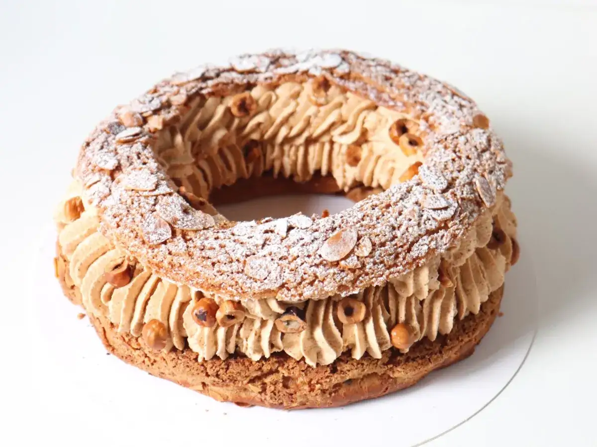 Un Paris-Brest craquelin, rond et g&eacute;n&eacute;reux, garni de cr&egrave;me pralin&eacute;e et parsem&eacute; d'amandes effil&eacute;es et de noisettes grill&eacute;es.
