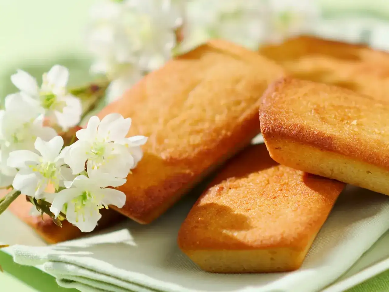 Financiers dorés, tout juste sortis du four à chaleur tournante, accompagnés de délicates fleurs blanches.