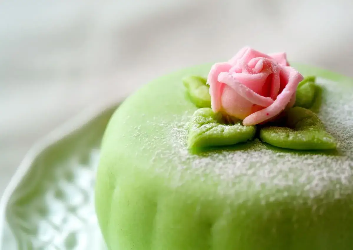 G&acirc;teau vert orn&eacute; d'une rose rose et de feuilles, saupoudr&eacute; de sucre glace. Un d&eacute;lice &agrave; la p&acirc;te d'amande.
