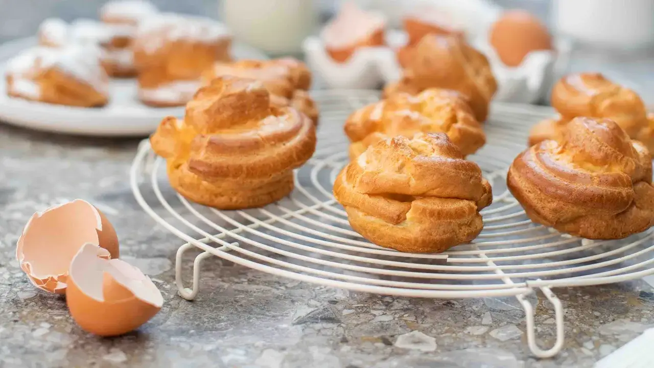 Petits choux dorés refroidissant sur une grille. La pâte à choux au robot a donné des merveilles, comme en témoignent les coquilles d'œufs à proximité.