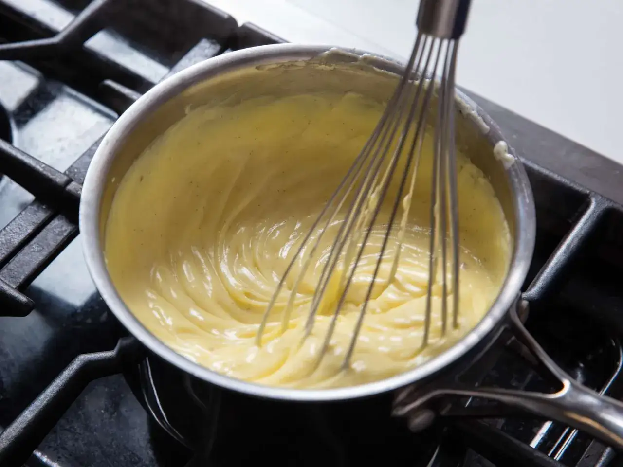 Une crème pâtissière mousseuse et onctueuse est fouettée dans une casserole sur une cuisinière.