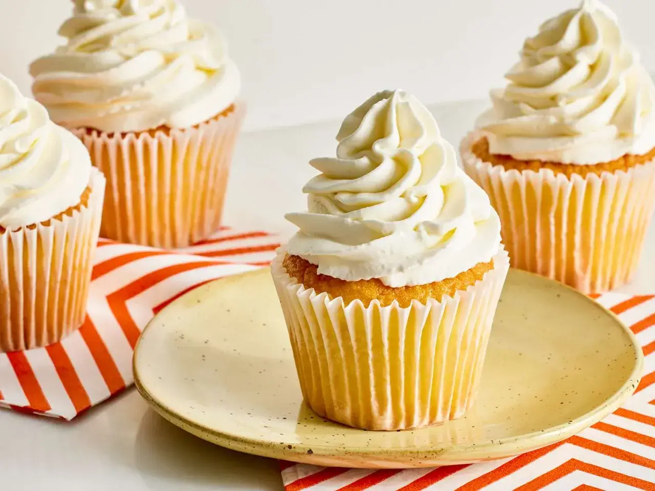 Quatre cupcakes décorés d'une généreuse crème fouettée épaisse, prêts à être dégustés.