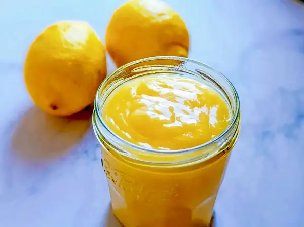 Un pot de crème citron onctueuse, parfaite pour une recette facile. Deux citrons frais à côté.