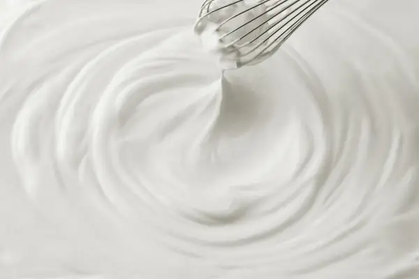 Un fouet mélangeant une crème chantilly aérienne, créant des tourbillons doux et onctueux.