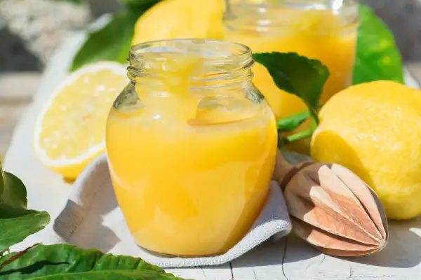 Un pot de crème au citron onctueuse, avec des citrons frais et une presse à bois. Parfait pour une tarte ou une crème dessert.