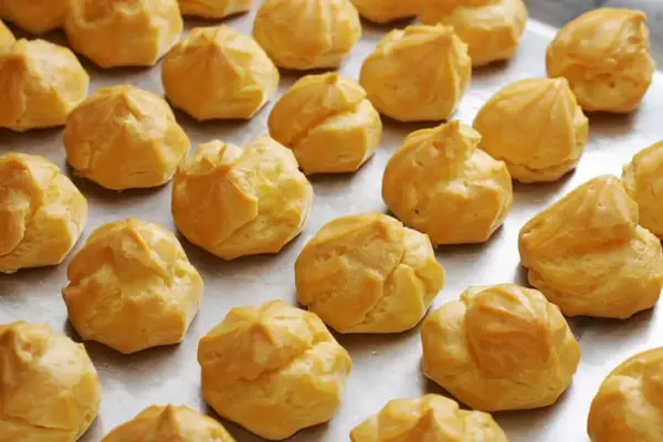 Une fournée de choux à la crème dorés, prêts pour la cuisson. Ils attendent patiemment d'être transformés en délices.