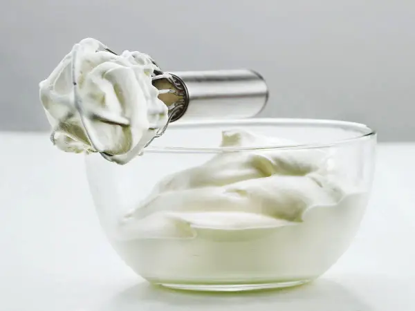 Crème fouettée aérienne prête à garnir un gâteau, dans un bol en verre.