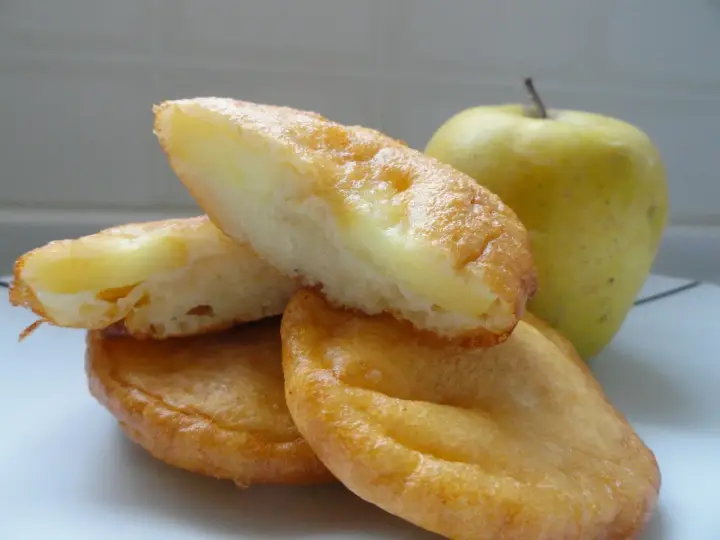 Délicieux beignets aux pommes au four, dorés et moelleux, avec une pomme verte en arrière-plan. Parfait pour une recette gourmande.