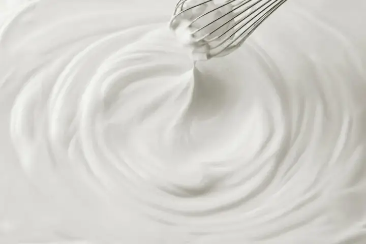 Un fouet mélangeant une crème chantilly aérienne, créant des tourbillons doux et onctueux.