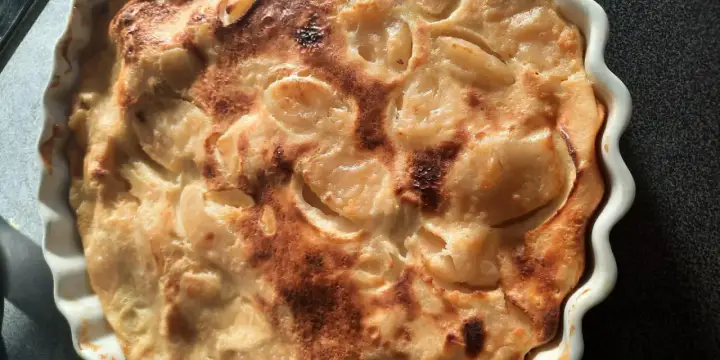 Un flan aux pommes normand doré et appétissant, tout juste sorti du four, dans un plat blanc festonné.