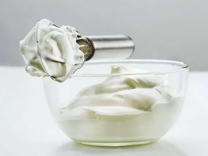 Crème fouettée aérienne prête à garnir un gâteau, dans un bol en verre.